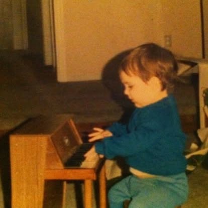 Topher as a young child playing a toy piano